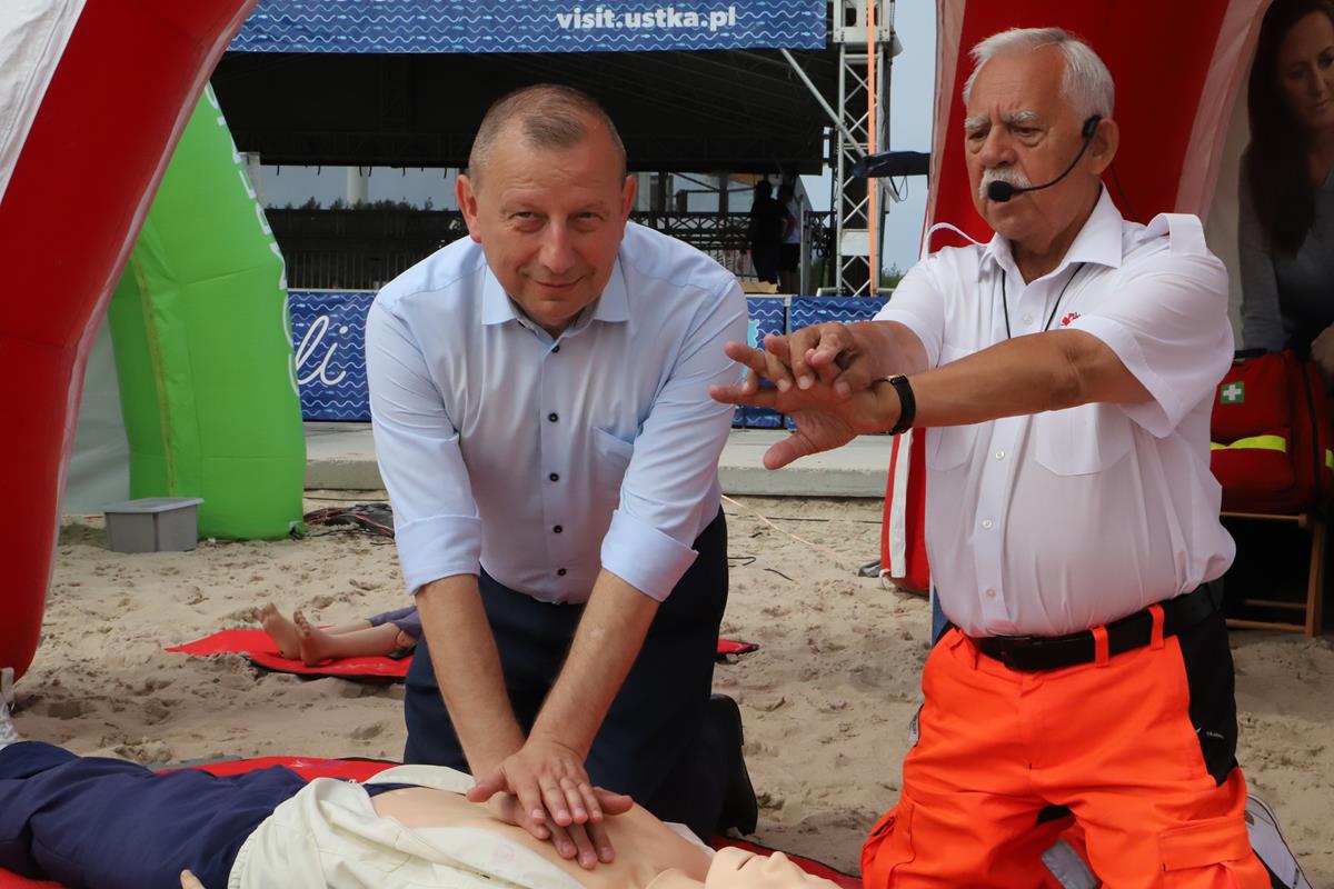 pokaz pierwszej pomocy, mężczyźni, manekin, w tle plaża