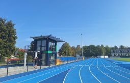 niebieska bieżnia na stadionie lekkoatletycznym, w tle las, obok bieżni wieża sędziowska
