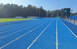 niebieska bieżnia na stadionie lekkoatletycznym, w tle las