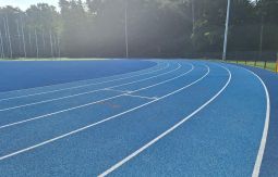 niebieska bieżnia na stadionie lekkoatletycznym, w tle las
